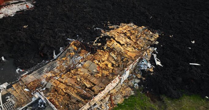 Drone close-up of a lava-destroyed home in Grindavik, Iceland, revealing exposed insulation, collapsed construction layers and black solidified basalt around the remaining footprint.