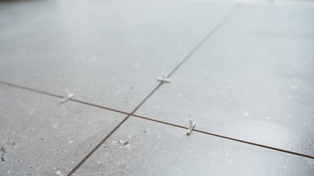 Close-up of gray floor tiles separated by cross spacers, showing straight intersecting grout joints and consistent gaps during installation.