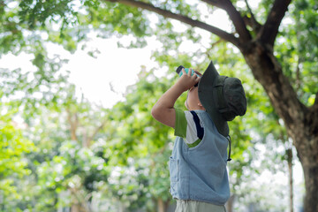 Fototapeta premium Side view of a little Asian boy looking up through binoculars to watch birds