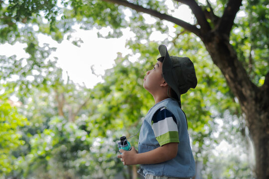 Side view of a cute young Asian boy wearing a hat and demin vest, looking up at tree