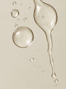 Clear cosmetic serum gel droplets and smear on beige background