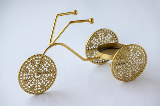 Golden metallic tricycle candle holder with ornate filigree wheel pattern isolated on white background, decorative home tabletop centerpiece.