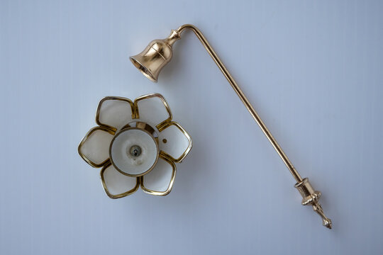 Top view of a brass candle snuffer with long handle next to a lotus flower shaped candle holder isolated on plain background.