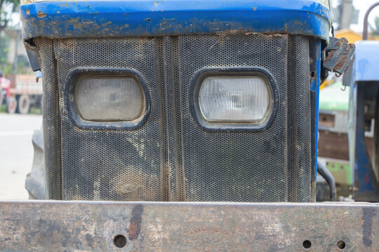 Front view close-up of an old blue tractor grille with dual rectangular headlights and rusty metal bumper.
