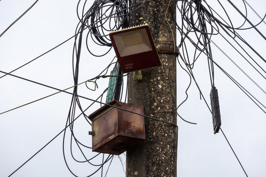 Close-up shot of an LED floodlight mounted on a concrete pole surrounded by messy tangled electrical wires.