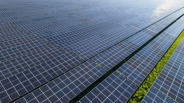 Aerial view of a large solar farm with rows of photovoltaic panels installed on a green field, capturing sustainable energy generation