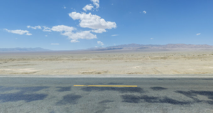 Empty Asphalt Highway Crossing Vast Desert Wilderness Under Blue Sky