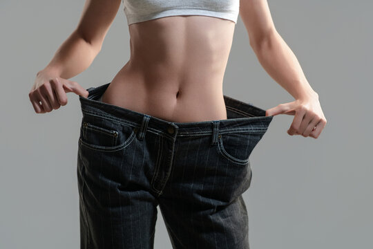 Slim figure in oversized jeans. Cropped slim figure with a bare waist. Slim figure and flat stomach closeup. Woman with a slim figure pulling jeans.