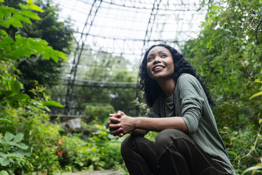 Smiling Woman Enjoying a Relaxing Moment Among Plants in a Botanical Dome