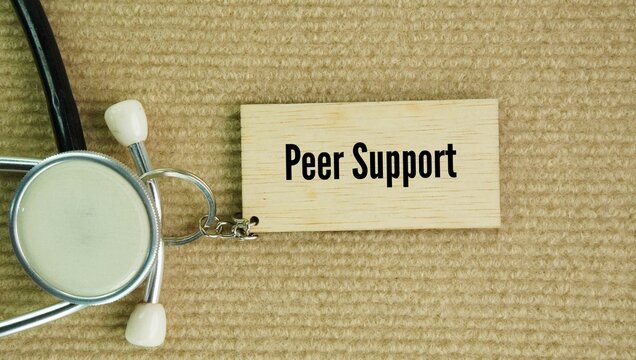 Stethoscope and wooden tag with the word Peer support is a system where people with similar life experiences give each other emotional, social, and practical help.