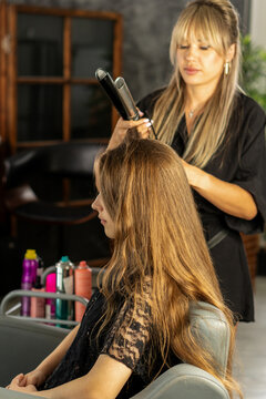 Hairstylist Straightening Hair Of Teen Client In Beauty Salon