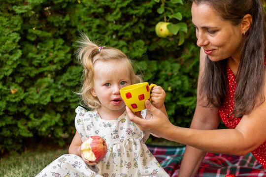 Young Daughter Holding Apple And Cup With Mother