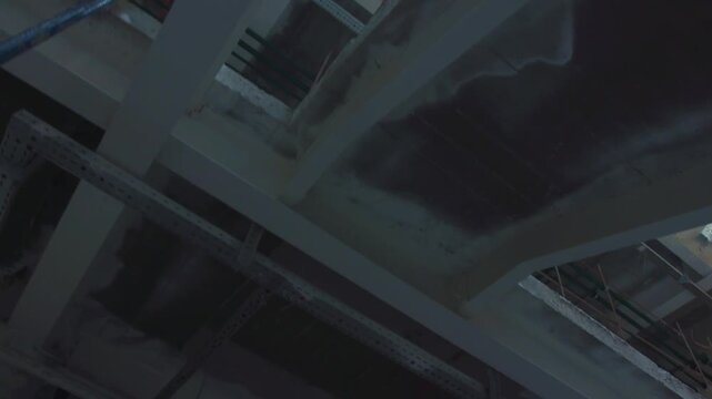 Unfinished commercial building interior space showing concrete structural beams exposed wiring and temporary metal scaffolding
