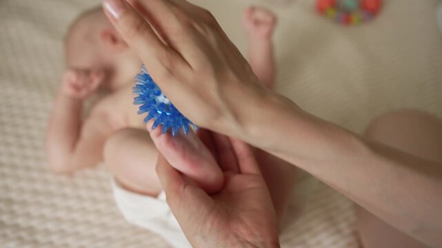 Careful mother giving a therapeutic foot massage to her infant child with a special spiky ball, promoting relaxation, physical development, and sensory stimulation for the newborn's well being