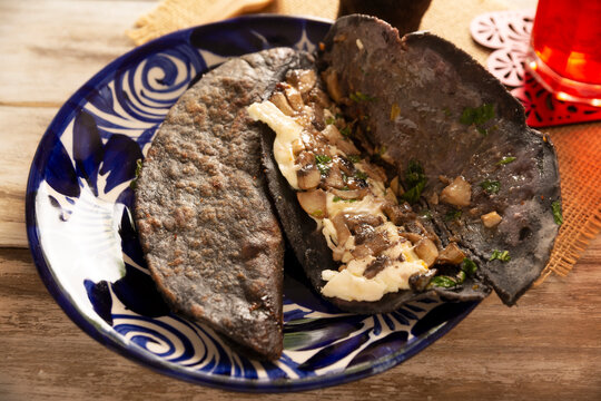 Mexican quesadillas made with blue corn tortillas filled with melted cheese and mushrooms served on a traditional plate and a glass of red hibiscus water (agua de jamaica) in the background.