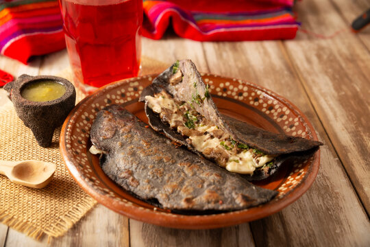 Mexican quesadillas made with blue corn tortillas filled with melted cheese and mushrooms served on a rustic clay plate and a glass of red hibiscus water (agua de jamaica) in the background.