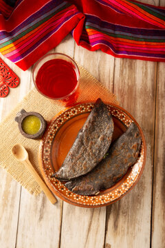 Mexican quesadillas made with blue corn tortillas filled with melted cheese and mushrooms served on a traditional plate and a glass of red hibiscus water (agua de jamaica) in the background.