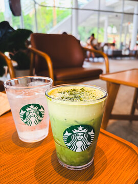 Bangkok, Thailand - September 14, 2026: Close up of a Starbucks iced matcha green tea latte and a cup of iced water on a wooden table in a brightly lit cafe.