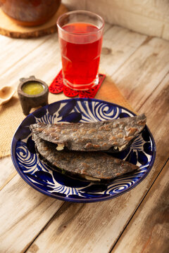Mexican quesadillas made with blue corn tortillas filled with melted cheese and mushrooms served on a traditional plate and a glass of red hibiscus water (agua de jamaica) in the background.