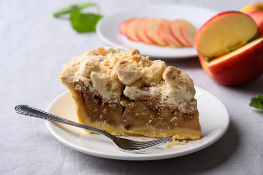 Apple crumble pie slice on white plate with fork and fresh apple fruit, autumn dessert for Thanksgiving and fall season
