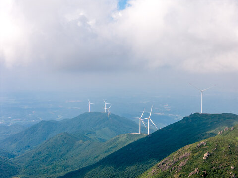 White wind turbines standing on rolling green mountains under cloudy sky