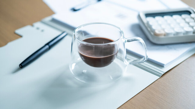 Coffee cup on financial documents with calculator and pen in background. Business accounting, budgeting, investment planning and office finance concept.
