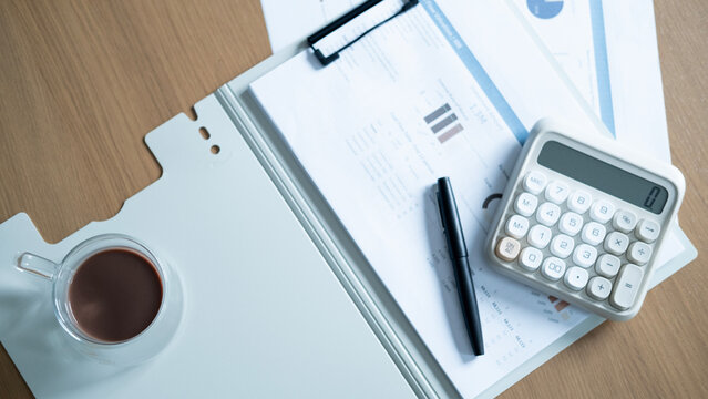 Financial planning workspace with calculator, coffee, pen and business reports on wooden desk. Accounting, budgeting, investment analysis and financial management concept.
