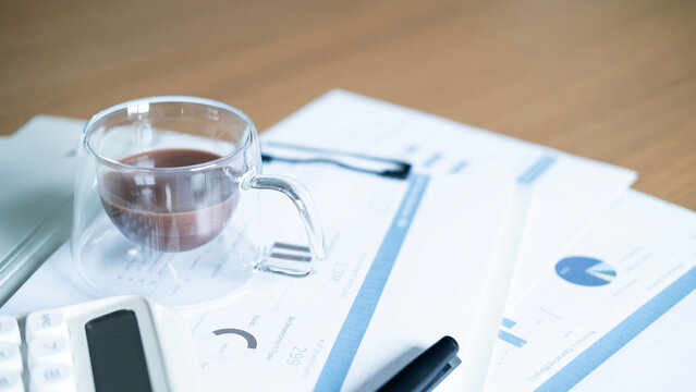 Coffee cup on business financial reports with calculator and pen. Investment analysis, accounting, budgeting and financial planning workspace concept.