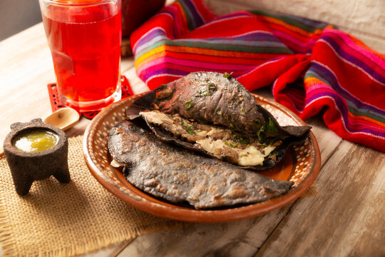 Mexican quesadillas made with blue corn tortillas filled with melted cheese and mushrooms served on a rustic clay plate and a glass of red hibiscus water (agua de jamaica) in the background.