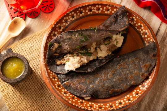 Mexican quesadillas made with blue corn tortillas filled with melted cheese and mushrooms served on a rustic clay plate and a glass of red hibiscus water (agua de jamaica) in the background.