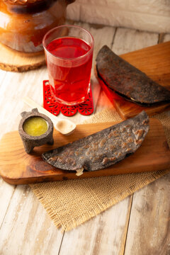 Mexican quesadillas made with blue corn tortillas filled with melted cheese and mushrooms served on a wooden cutting board and a glass of red hibiscus water (agua de jamaica) in the background.