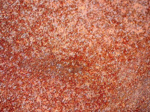 Close-up of rust and corrosion covering a metal sheet, creating a rough orange brown texture and industrial background showing oxidation, weathering and material deterioration.