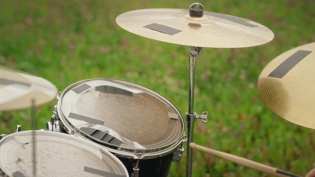 Person playing acoustic drum kit with sticks outdoors during music rehearsal. Suitable for indie band promotions, music festival ads and youth lifestyle content