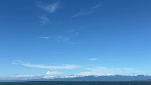 岬と山のシルエットが遠くに見える穏やかな夏の海辺の景色