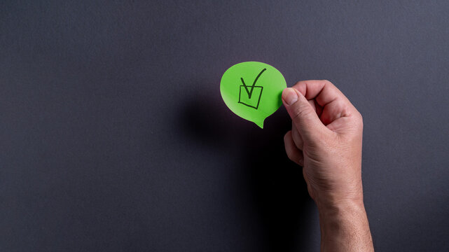 Male hand holding green speech bubble with check mark on dark background