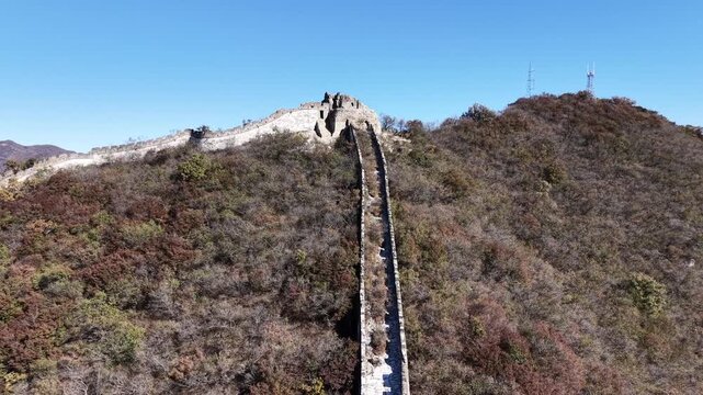 Static side aerial view of the Great Wall climbing steeply up a mountain slope, the narrow stone path ascending toward the summit with autumn brown hillside on both sides, Huairou, Beijing, China.