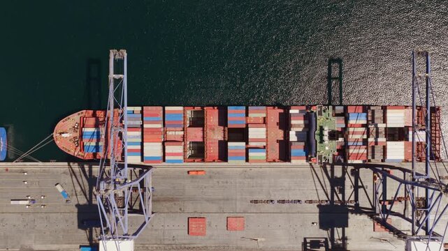 Aerial top-down view of gantry cranes loading and unloading colorful cargo containers on a large vessel docked at a commercial shipping port, illustrating global trade and logistics