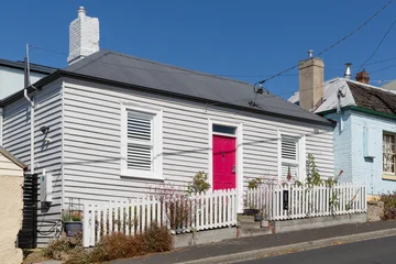 Weatherboard cottage painted grey with a bright red front door and a white picket fence © Steve Lovegrove