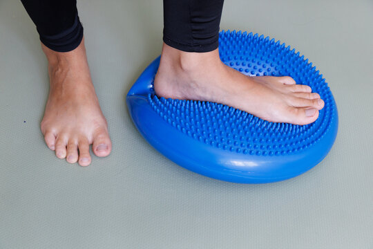 One foot loads a massage balance cushion during preventive physiotherapy to train plantar pressure, ankle control, proprioception and foot arch stability.