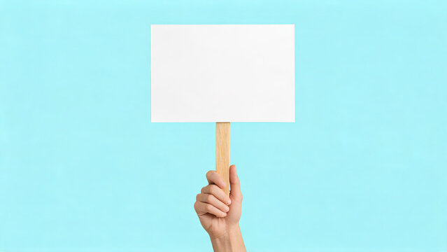 A person's hand holds a blank white placard mounted on a wooden stick, set against a solid light blue background.