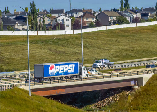 Calgary, AB, Canada - Sept 13, 2026: A Pepsi delivery truck drives across an overpass bridge in front of suburban houses on a sunny day.