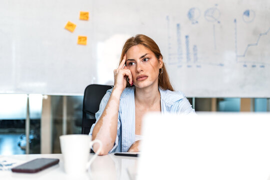 Thoughtful young woman sitting at office desk with laptop. Tired female employee thinking about business strategy while working indoors. Professional corporate lifestyle concept.