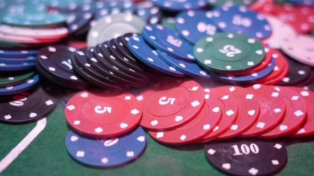 Close-up of assorted poker chips. Blue chips marked 50. Red chips show 25. Green chips have 100. Black chips with white dots. Blurred casino background. Vibrant colors indicate gambling