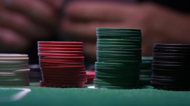 Green felt casino table holds neatly stacked poker chips. Red, green, and black chips form tight columns. Close-up captures high stakes gambling atmosphere. Ideal for poker or casino scene usage