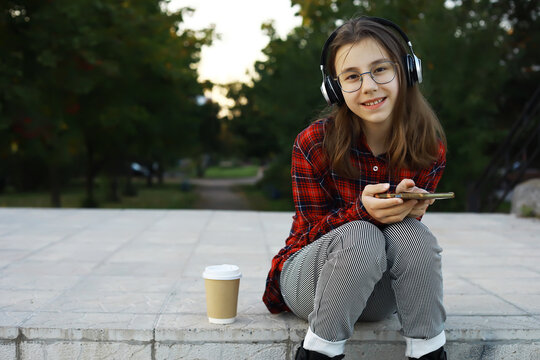 Young Girl Enjoying Music on Headphones Outdoors with Phone and Coffee Cup