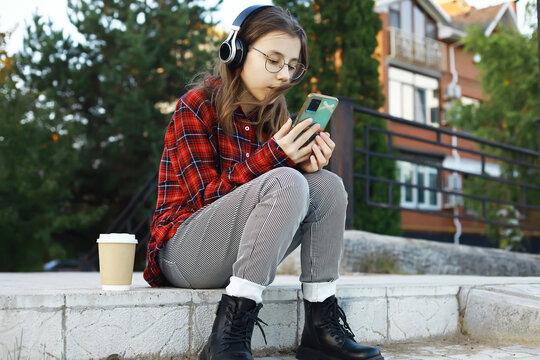 Teen Girl Relaxing Outdoors with Coffee, Headphones, and Smartphone