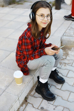 Young Girl in Plaid Shirt Listening to Music with Headphones Outdoors