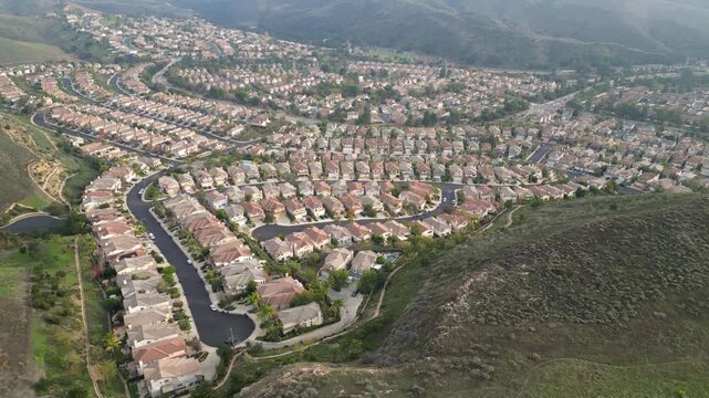Aerial drone view moving backwards over upscale suburban tract homes in the Lang Ranch neighborhood of Thousand Oaks, California, on an overcast January day, 2024.