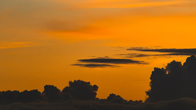Silhouetted Clouds Against Bold Orange Sunset Gradient Sky