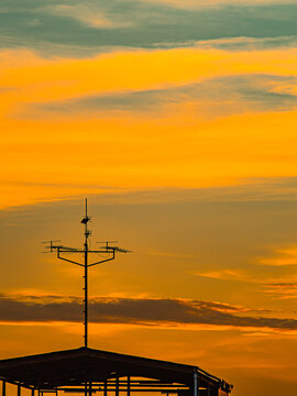 Silhouette of Rooftop TV Antennas Against Vivid Orange Sunset Sky
